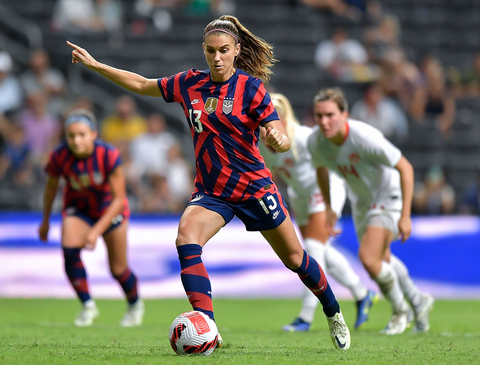 A female soccer player from the U.S. Women's National Team, skillfully dribbling the ball in a vibrant red and blue striped jersey.