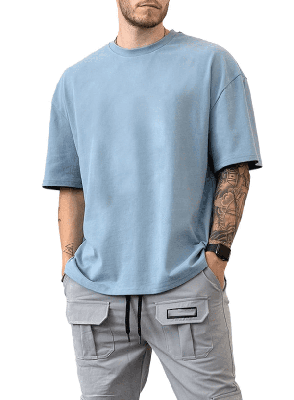 Man wearing light blue oversized t-shirt and gray cargo pants with smartwatch and tattoo on arm.