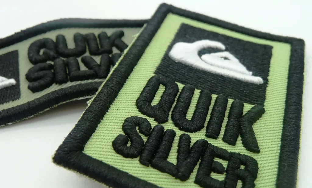 Quiksilver embroidered patch showcasing the brand's logo on a green background, perfect for custom clothing.