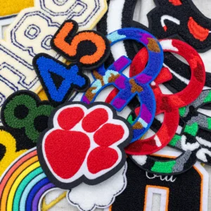 A variety of colorful embroidered patches featuring numbers, a paw print, and a rainbow design, perfect for adding custom details to apparel and accessories.
